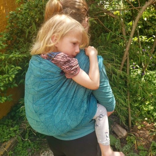sad looking white , blonde haired 6 yr old being back carried in a woven wrap