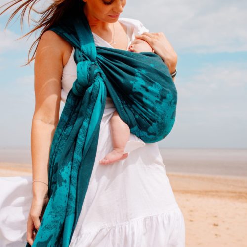 family on the beach with baby carried in a teal and navy woven wrap with a sea design