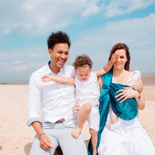 family on the beach with baby carried in a teal and navy woven wrap with a sea design