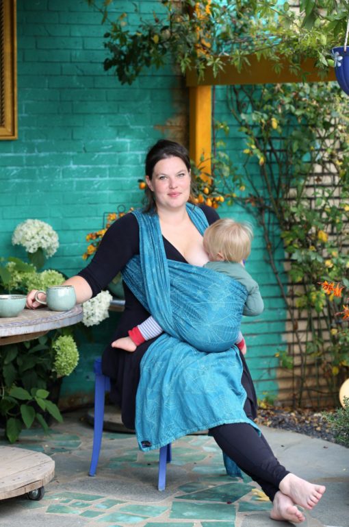 teal and turquoise woven warp with a cobweb design worn in a front carry nursing a toddler