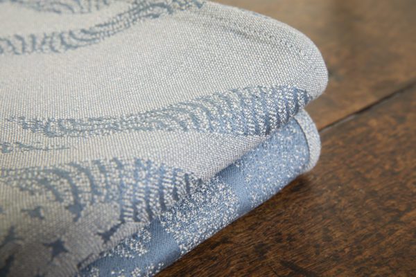 A woven wrap with a pale grey and grey-blue design showing starling murmuration over a wintery treeline