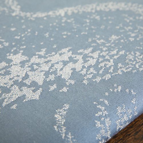 A woven wrap with a pale grey and grey-blue design showing starling murmuration over a wintery treeline