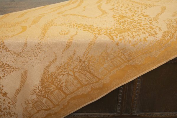 A woven wrap that has a shimmery pale grey linen and merino blend weft against a mustard-gold organic cotton warp. Our Murmuration design shows a starling murmuration over a wintery treeline