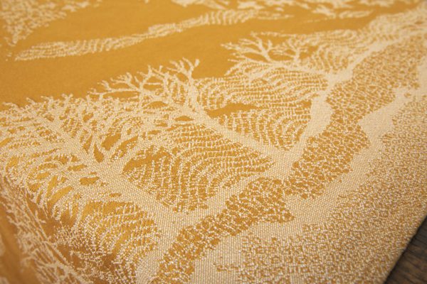 A woven wrap that has a shimmery pale grey linen and merino blend weft against a mustard-gold organic cotton warp. Our Murmuration design shows a starling murmuration over a wintery treeline