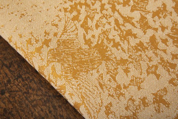 A woven wrap that has a shimmery pale grey linen and merino blend weft against a mustard-gold organic cotton warp. Our Murmuration design shows a starling murmuration over a wintery treeline