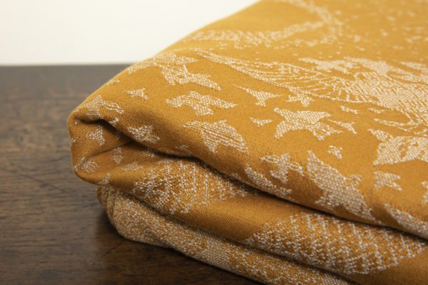 A woven wrap that has a shimmery pale grey linen and merino blend weft against a mustard-gold organic cotton warp. Our Murmuration design shows a starling murmuration over a wintery treeline
