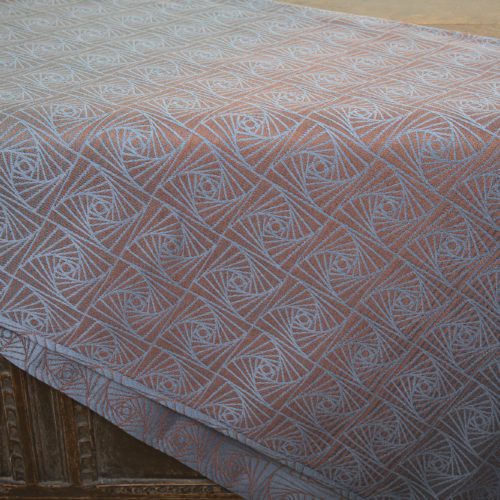 A woven wrap with a geometric design in a gradient of russet and brown shimmery linens against a grey-blue cotton