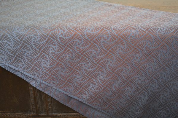 A woven wrap with a geometric design in a gradient of russet and brown shimmery linens against a grey-blue cotton