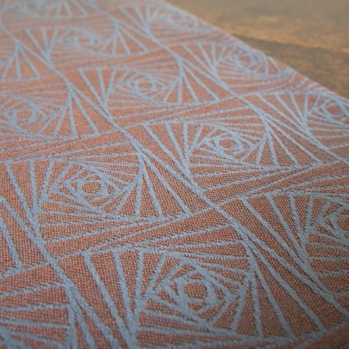 A woven wrap with a geometric design in a gradient of russet and brown shimmery linens against a grey-blue cotton