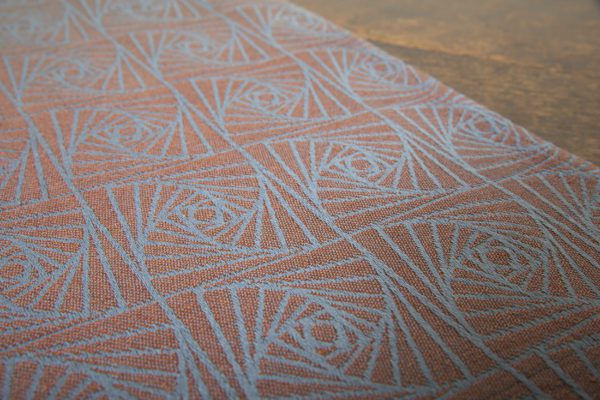 A woven wrap with a geometric design in a gradient of russet and brown shimmery linens against a grey-blue cotton