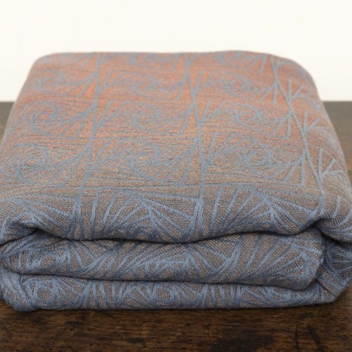 A woven wrap with a geometric design in a gradient of russet and brown shimmery linens against a grey-blue cotton