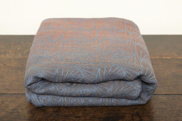 A woven wrap with a geometric design in a gradient of russet and brown shimmery linens against a grey-blue cotton