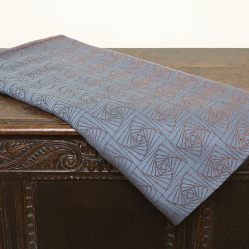 A woven wrap with a geometric design in a gradient of russet and brown shimmery linens against a grey-blue cotton