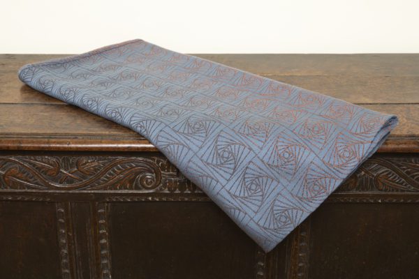 A woven wrap with a geometric design in a gradient of russet and brown shimmery linens against a grey-blue cotton