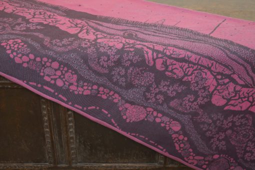 A flat shot of a woven wrap sling with a bright pink and dark grey design of a rainy hillside with fossils and fractals and pylons