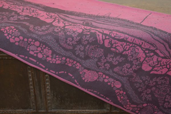 A flat shot of a woven wrap sling with a bright pink and dark grey design of a rainy hillside with fossils and fractals and pylons