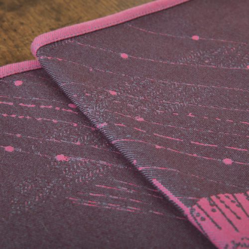 A flat shot of a woven wrap sling with a bright pink and dark grey design of a rainy hillside with fossils and fractals and pylons