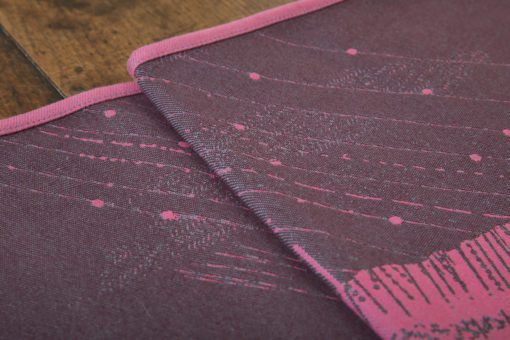 A flat shot of a woven wrap sling with a bright pink and dark grey design of a rainy hillside with fossils and fractals and pylons
