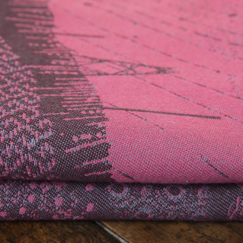 A flat shot of a woven wrap sling with a bright pink and dark grey design of a rainy hillside with fossils and fractals and pylons