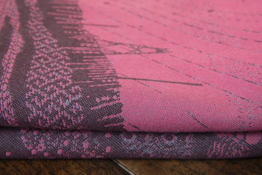 A flat shot of a woven wrap sling with a bright pink and dark grey design of a rainy hillside with fossils and fractals and pylons