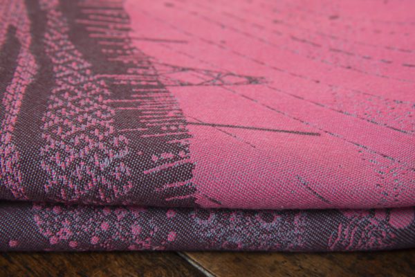 A flat shot of a woven wrap sling with a bright pink and dark grey design of a rainy hillside with fossils and fractals and pylons