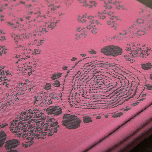 A flat shot of a woven wrap sling with a bright pink and dark grey design of a rainy hillside with fossils and fractals and pylons