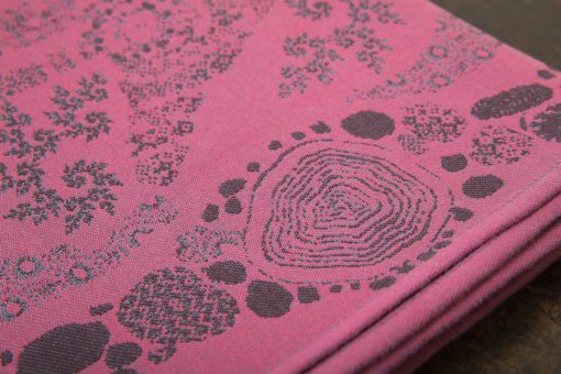 A flat shot of a woven wrap sling with a bright pink and dark grey design of a rainy hillside with fossils and fractals and pylons