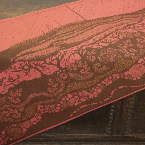 A woven wrap with a warm salmon pink and dark brown design of a rainy hillside with fossils and fractals underground and pylons above