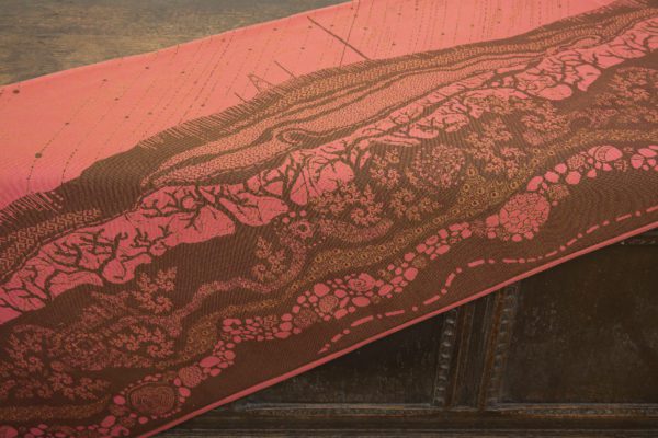 A woven wrap with a warm salmon pink and dark brown design of a rainy hillside with fossils and fractals underground and pylons above