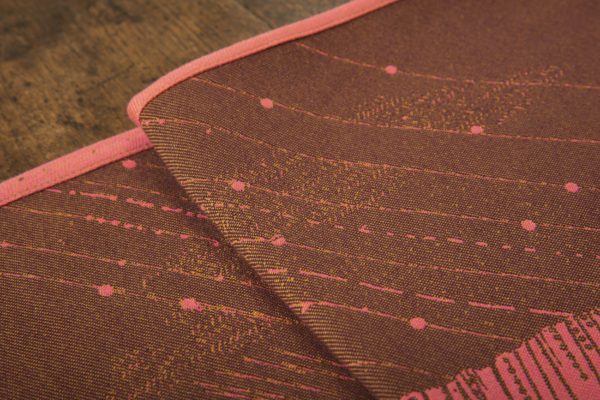 A woven wrap with a warm salmon pink and dark brown design of a rainy hillside with fossils and fractals underground and pylons above