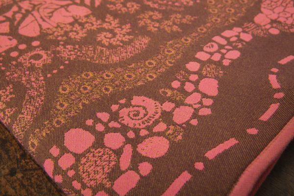 A woven wrap with a warm salmon pink and dark brown design of a rainy hillside with fossils and fractals underground and pylons above