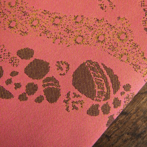 A woven wrap with a warm salmon pink and dark brown design of a rainy hillside with fossils and fractals underground and pylons above