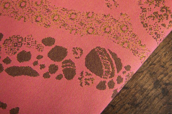 A woven wrap with a warm salmon pink and dark brown design of a rainy hillside with fossils and fractals underground and pylons above