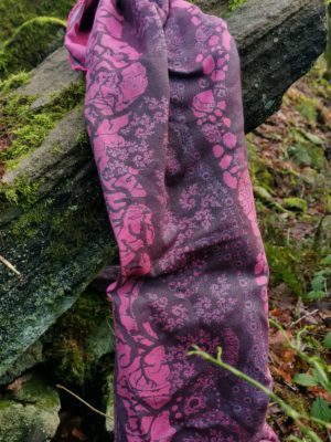 A flat shot of a woven wrap sling with a bright pink and dark grey design of a rainy hillside with fossils and fractals and pylons