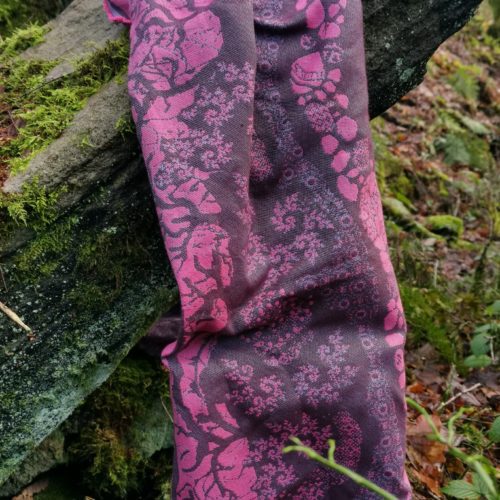 A flat shot of a woven wrap sling with a bright pink and dark grey design of a rainy hillside with fossils and fractals and pylons