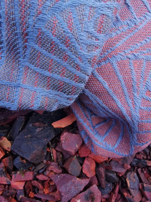 A woven wrap with a geometric design in a gradient of russet and brown shimmery linens against a grey-blue cotton